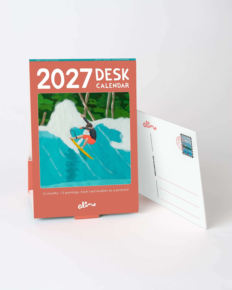 Small standing desk calendar for 2027 on a desk, next to an art card showing its postcard back