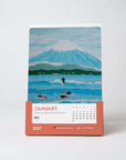 January card of the Alimo 2027 art desk calendar, an original painting of surfers below a snowy peak in Japan
