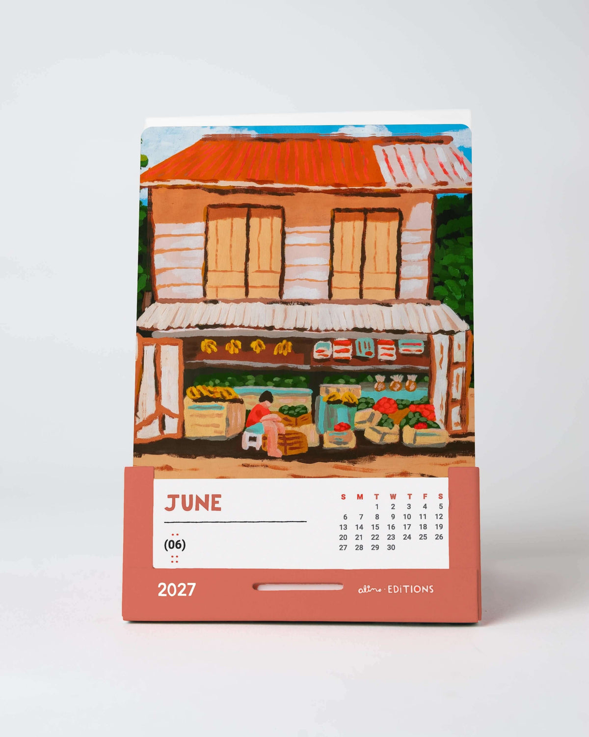June card of the 2027 desk calendar standing on a desk, an original painting of a corner grocery store