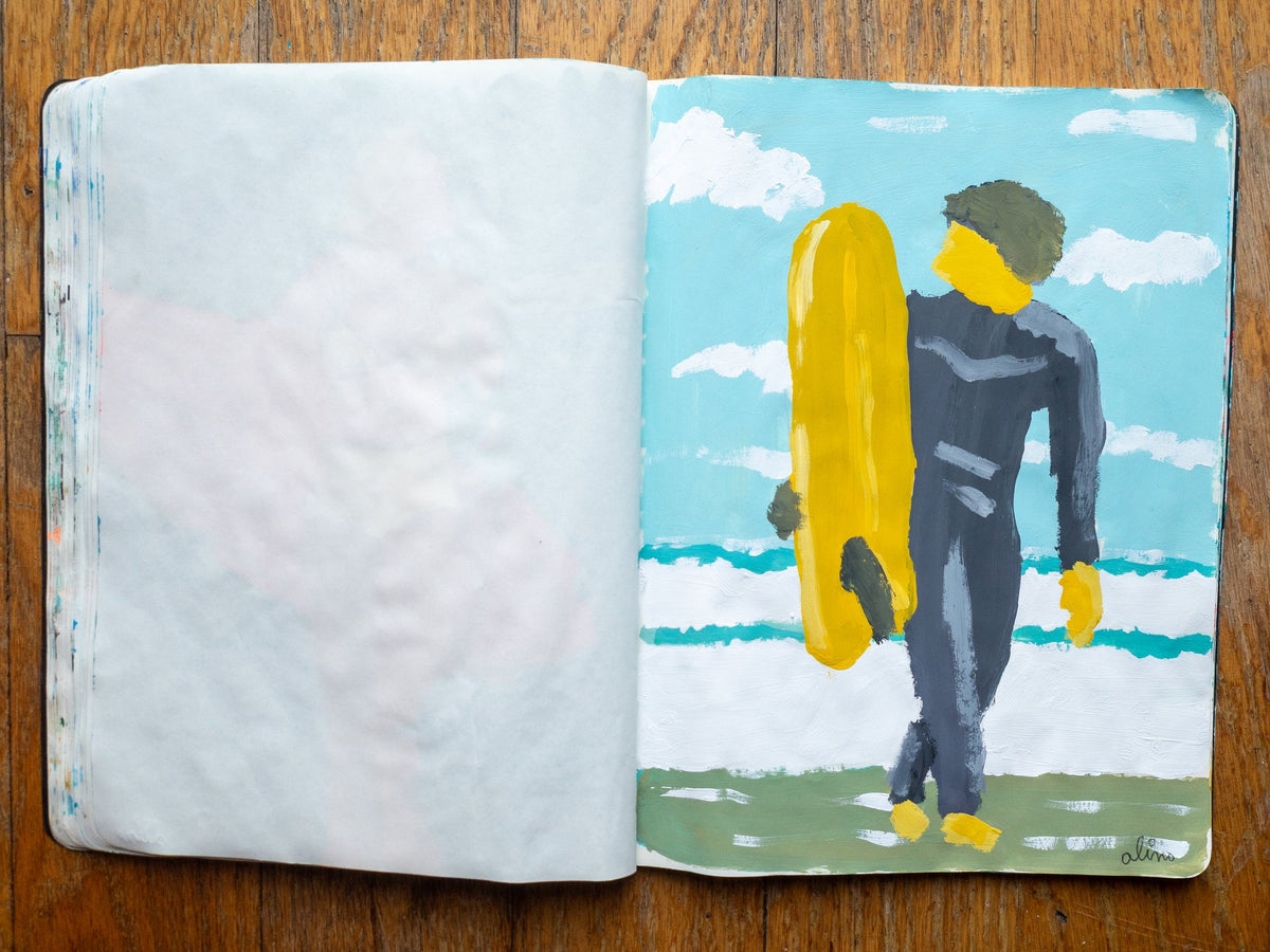 Drop 07 sketch 01 by Alimo in the open Moleskine sketchbook, painted on the right page only: a surfer in a dark wetsuit carrying a yellow surfboard up the beach